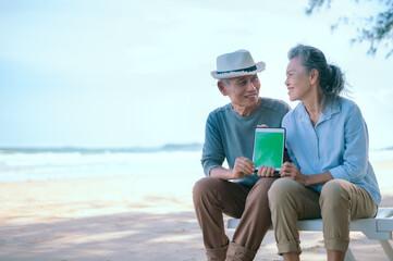 Elderly Asian couple holding laptops green sceen on the beach