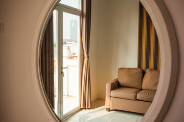 A cute and cozy room interior reflected in a big oval mirror hanging on the wall. A nice and...