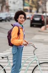 African american woman with backpack standing near bicycle on urban street