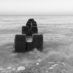 Black and white photograph of groynes at the north beach in Bridlington at dawn, with motion blur of the waves.