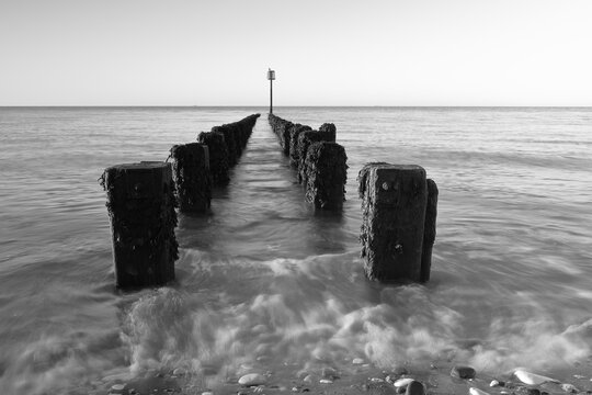 Black and white photograph of groynes at the north beach in Bridlington at dawn, with motion blur of the waves.