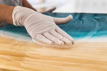 Female artist in protective gloves spreading white epoxy resin onto turquoise color