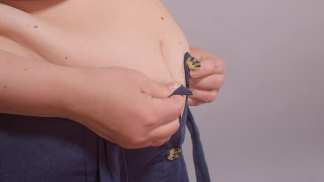 A woman with a fat belly tries to button up small clothes. Weight gain of a person in life. Excess weight.