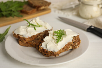 Bread with cream cheese and arugula on white wooden table