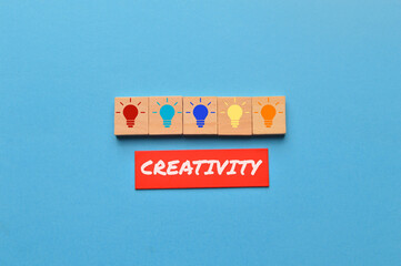 Light bulb on wooden blocks and the word CREATIVITY