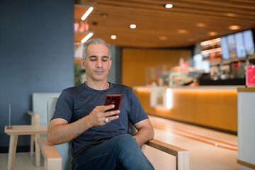 Portrait of handsome man sitting at coffee shop using mobile phone