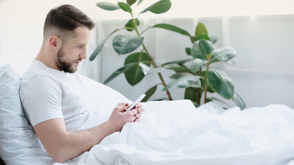 young bearded man using smartphone in bed.