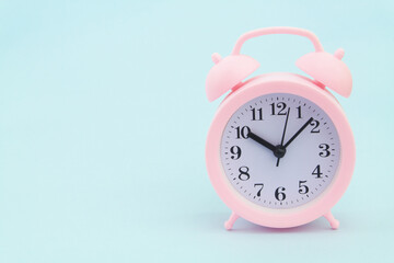 Pink alarm clock on blue background, large space for text.	