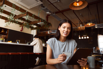 Portrait of woman in coffee shop with digital tablet making online transaction using credit card