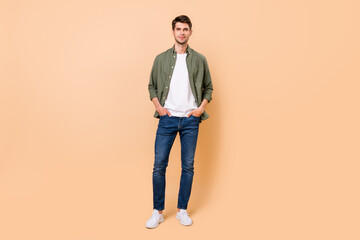 Photo of charming confident young guy dressed green shirt smiling walking arms pockets isolated...