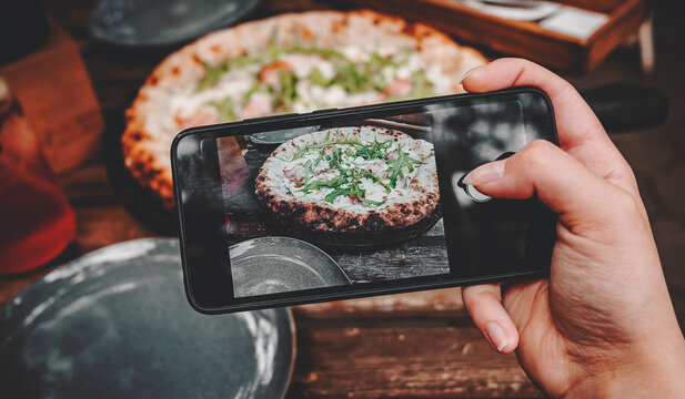 woman hand with smartphone photographing pizza at restaurant or cafe