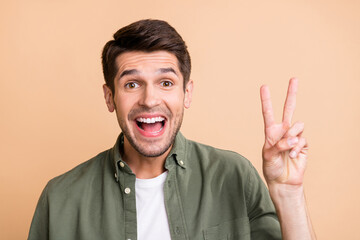 Photo of charming happy positive young man good mood make v-sign isolated on beige color background