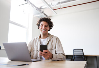 Young man with laptop and mobile phone at desk working on start up business in open plan office