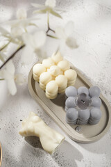 Two grey-blue and white bubble candles on a concrete tray on pastel background, a close up