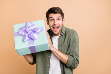Photo of amazed charming happy young man hold hands gift curious present isolated on beige color...