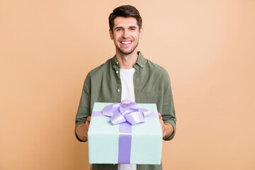 Photo of charming happy young man give gift box you smile celebrate holiday isolated on beige color...