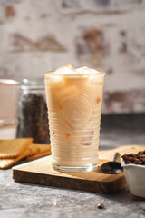 A glass with ice cubes and milk coffee on a wooden board