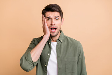 Photo of tired shocked young guy dressed green shirt arm cheek open mouth isolated beige color background