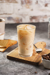 A glass with ice cubes and milk coffee on a wooden board