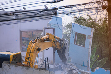 big yellow excavator removal home building by destroy blue concrete wall. uproot old construction...