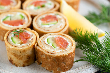 Crepe salmon rolls with cucumber and cream cheese on a plate, closeup view. Gourmet appetizer