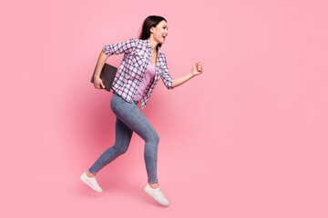 Full length photo of pretty shiny young woman wear plaid shirt jumping holding modern device empty space isolated pink color background