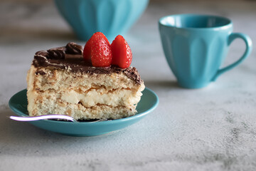 Meringue cake with cream on a blue saucer and a blue cup with coffee on a gray background.
