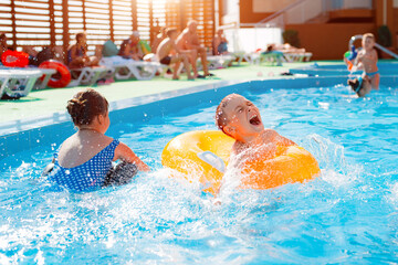 Kid boy playing outdoor pool of resort. in an inflatable yellow circle with a ball. Children frolic...