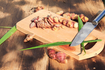 sliced ​​red ginger with fresh lemongrass stalks on a placemat with a wooden backdrop