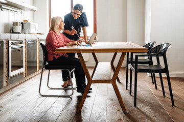 A side view of positive female doctor showing something in laptop to her smiling elderly patient