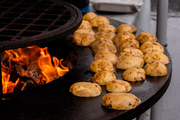 Process of cooking yellow potatoes on grill at summer outdoor food market - close up. Professional cooking, catering, cookery, barbecue, gastronomy and street food concept