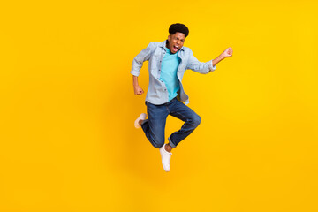 Fototapeta na wymiar Photo of funky excited dark skin man wear jeans shirt jumping high running fast isolated yellow color background