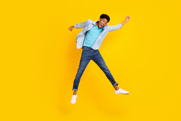 Fototapeta na wymiar Photo of attractive lucky dark skin guy dressed denim shirt rising fists jumping high isolated yellow color background