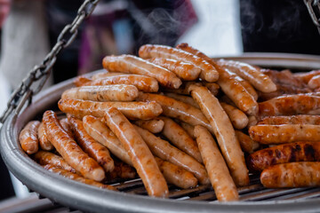 Close up: process of grilling fresh meat sausages on big round hanging grill at summer local food market. Outdoor cooking, barbecue, gastronomy, cookery, street food concept