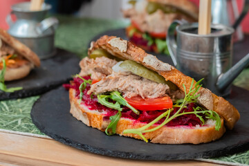 Sandwich with tuna, arugula, pickle, tomato, beetroot on counter at summer local food market - close up. Gastronomy, street food, mediterranean and Italian dish concept