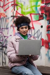 Young african american woman using laptop near graffiti outdoors
