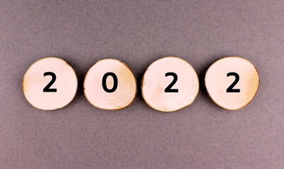 The inscription 2022 on round sawn off wooden discs on a gray background. Round wooden blanks with numbers - obrazy, fototapety, plakaty