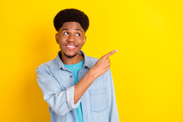 Photo of funky dreamy dark skin guy dressed denim shirt smiling looking pointing finger empty space isolated yellow color background