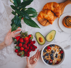 Breakfast food with woman hands, Mini pancakes with strawberries, croissants and avocado, Delicious summer food, Top view on a light marble background