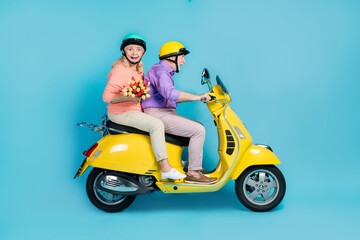 Full body profile side photo of retired grey haired pensioner couple ride bike hold tulips date isolated on blue color background