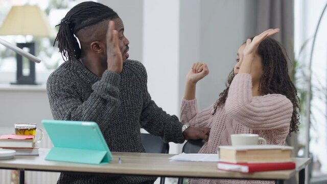 Cheerful African American teen daughter giving high-five to smiling father helping student with homework at home. Positive happy cute teen and handsome confident man rejoicing task decision