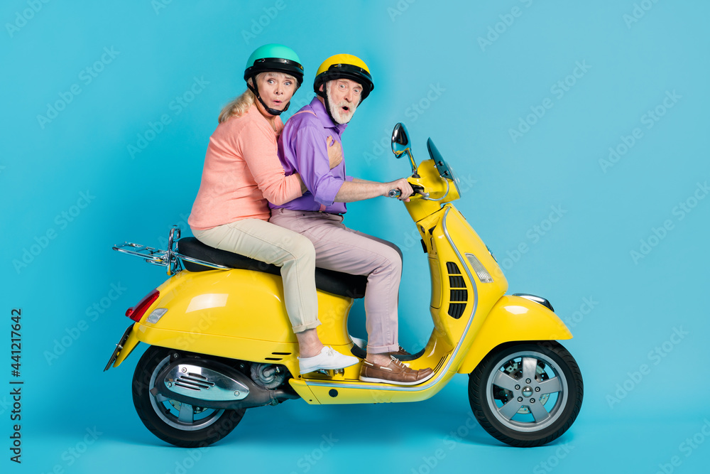 Poster Portrait of two amazed elderly retired pensioners riding moped pout lips weekend isolated over bright blue color background