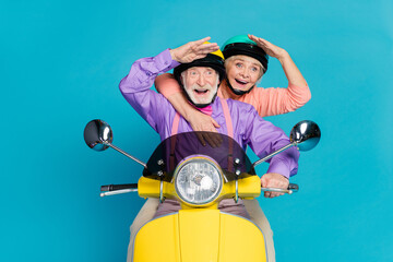 Portrait of two nice elderly retired pensioner friends riding bike looking far away having fun isolated over bright blue color background