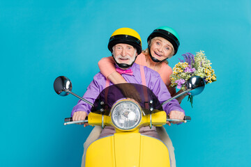 Photo of retired pensioner grey haired husband wife couple hold flowers ride bike isolated on blue...