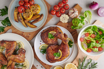 Grilled chicken wings, grilled chicken legs in barbecue sauce and roasted vegetables and mixed vegetable salad with tomatoes, lemon in white plate on light color stone table. Top view, Flat lay..
