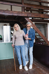 Fototapeta premium Senior woman with crutch standing near careful husband at home