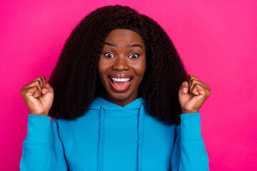 Photo of charming lucky dark skin woman dressed blue sweatshirt smiling rising fists isolated pink...