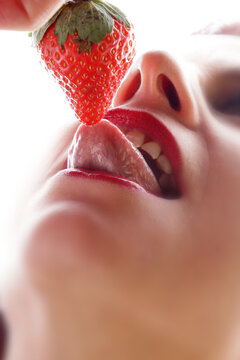 Eine Frau leckt mit der Zunge an einer roten Erdbeere