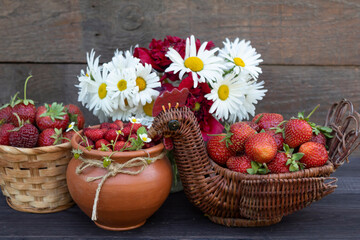 Obraz na płótnie Canvas a pot with wild strawberries, wicker vases with strawberries and a bouquet of daisies and poppies