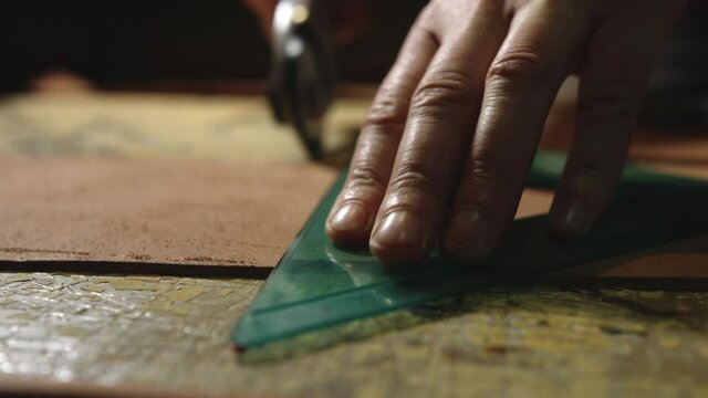 Leather craftsman at work. Close up of his hands cutting leather towards the camera with a rotating knife and a bracket
